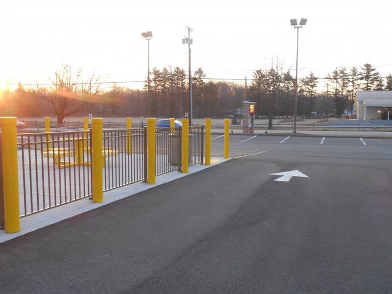 Parking lot with yellow bollards, fenced walkway, and directional arrow at sunset