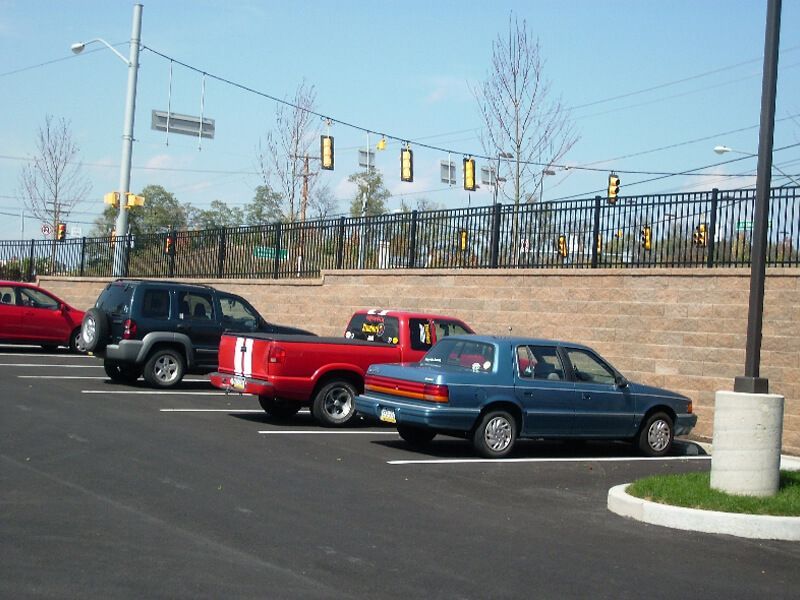 Cars parked in a lot beside a brick wall and traffic lights under a clear sky.