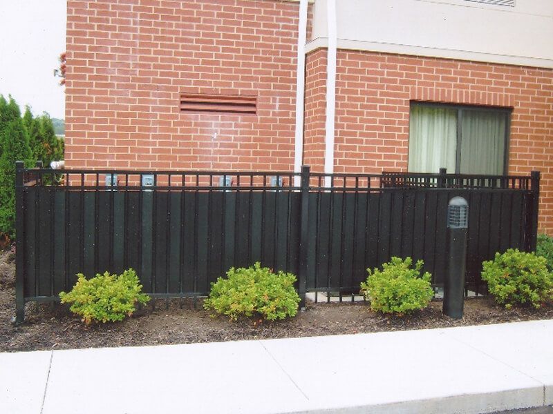 Black metal fence in front of a brick house with small shrubs and a sidewalk