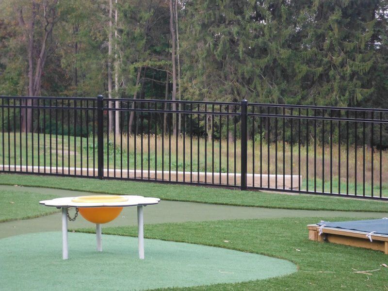 Small outdoor patio with a white table, orange object underneath, fence, grass, and trees in the background