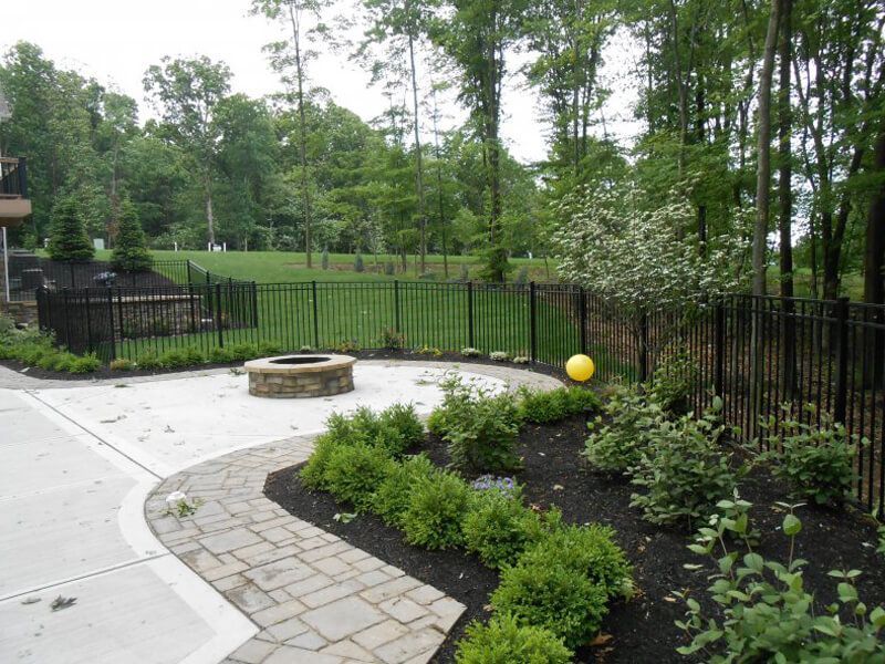 Backyard patio with stone path, black fence, shrubs, and a yellow ball near the garden bed.