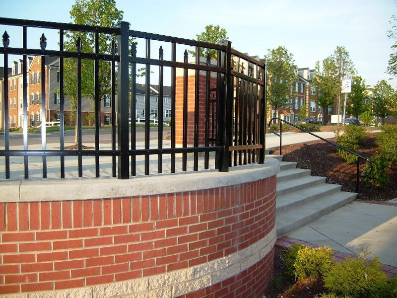 Brick curved wall with black metal fence beside steps in a landscaped urban park