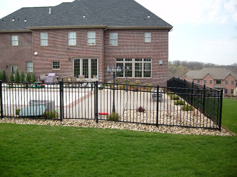 Backyard patio with black metal fence, stone landscaping, and a large brick house