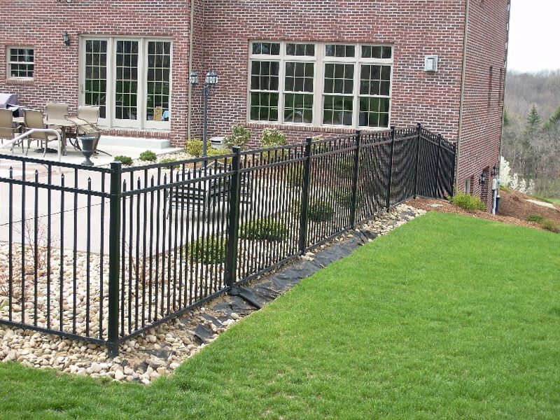 Brick house patio with black metal fence and green lawn bordered by rocks