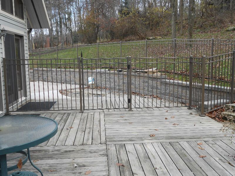 Wooden deck with metal gate and railing overlooking a yard and wooded hillside