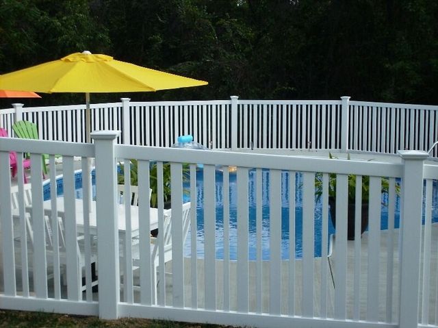 Backyard pool with white fence and yellow umbrella, blue float visible in the water.