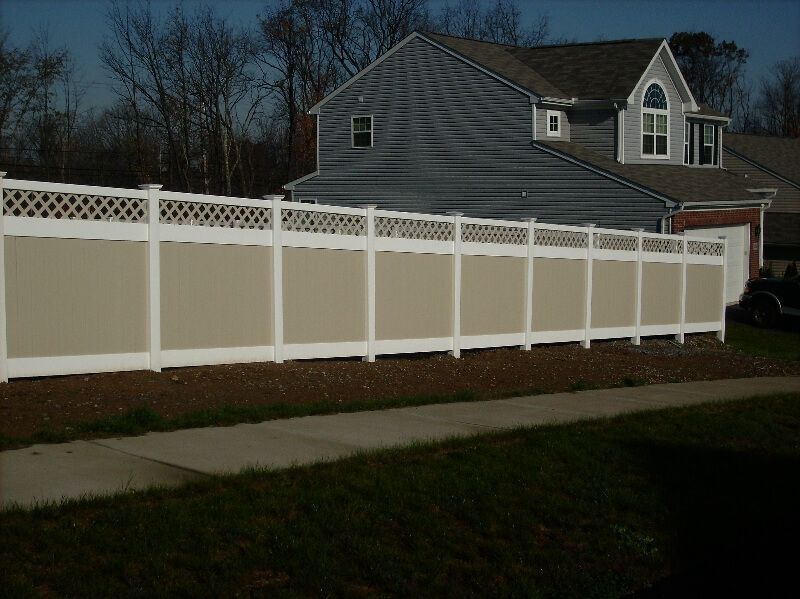White vinyl privacy fence with lattice top in front of a gray house at dusk