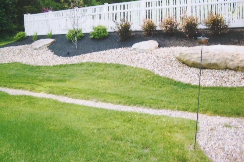 Landscaped yard with green lawn, gravel beds, shrubs, and a white fence along the back.