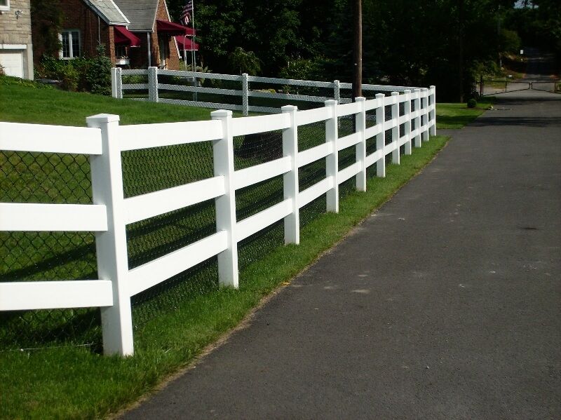 White wooden fence lining a paved road beside a grassy yard and houses