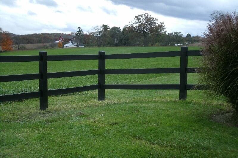 Black wooden fence across a green grassy field under a cloudy sky