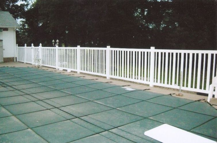 White fence along a green-paved outdoor patio beside trees at dusk