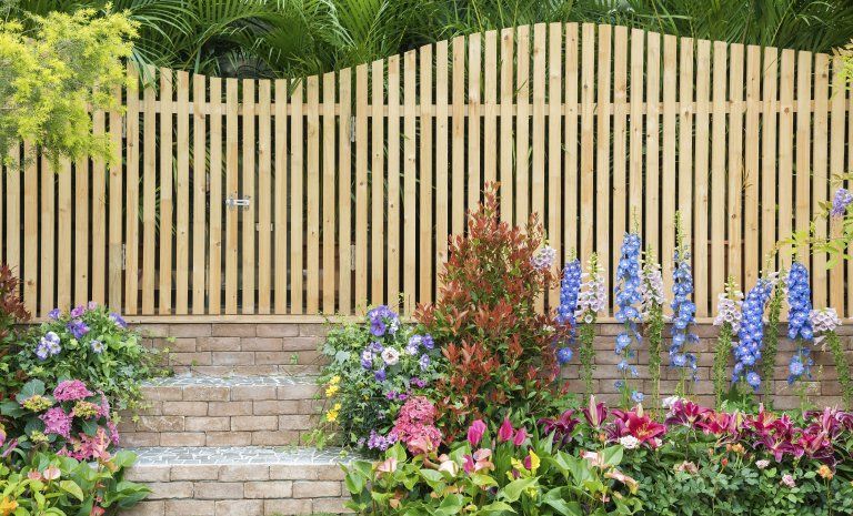 Curved wooden garden fence behind stone steps, bordered by colorful blooming flowers and greenery