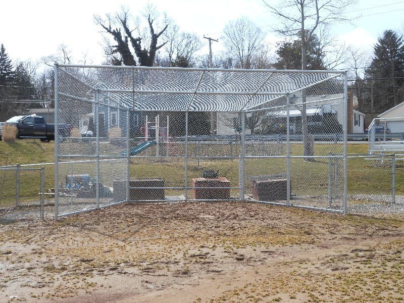 Chain-link baseball batting cage with a dirt floor in a park