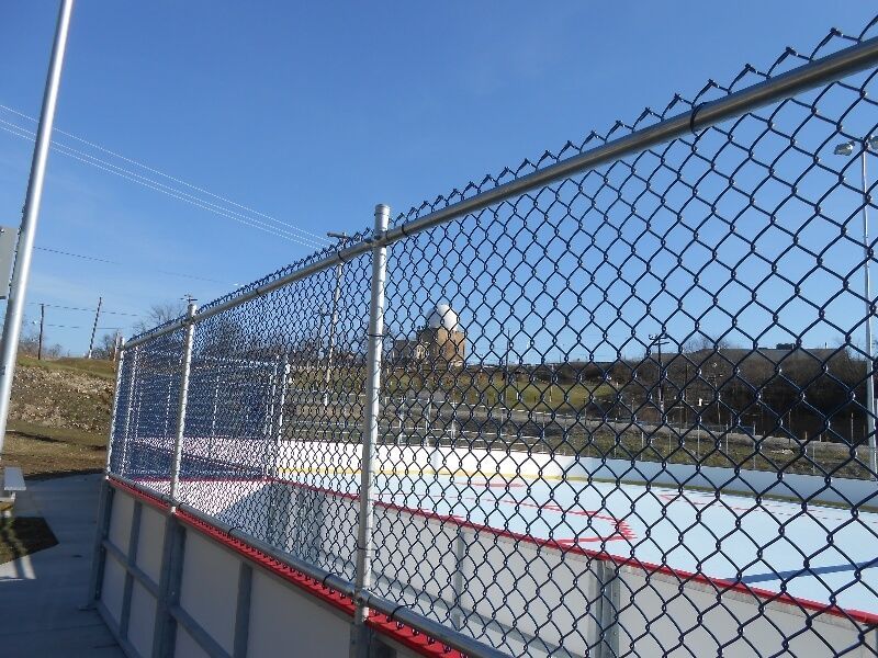 Chain-link fence beside an outdoor ice rink under a clear blue sky.