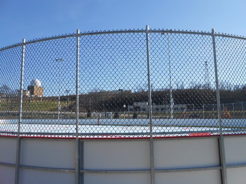 Chain-link fence around an outdoor hockey rink under a blue sky