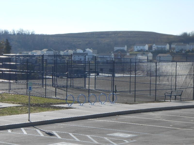 Empty outdoor court with blue fencing, metal gates, and houses on a hill in the background
