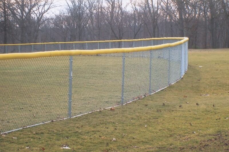 Curved chain-link fence with yellow top rail along a grassy field under bare trees