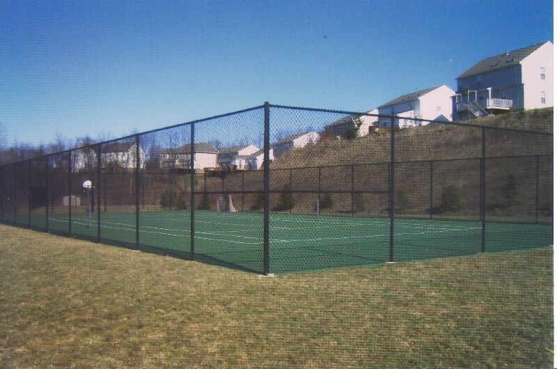 Outdoor tennis court with black chain-link fencing and grassy surroundings under a clear blue sky