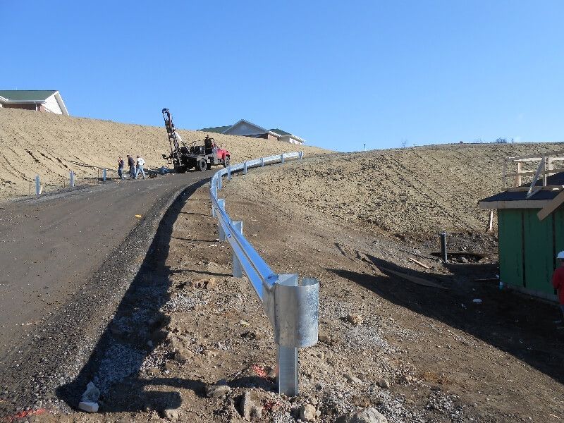 Curving paved road with metal guardrail on a barren hillside under a clear blue sky.