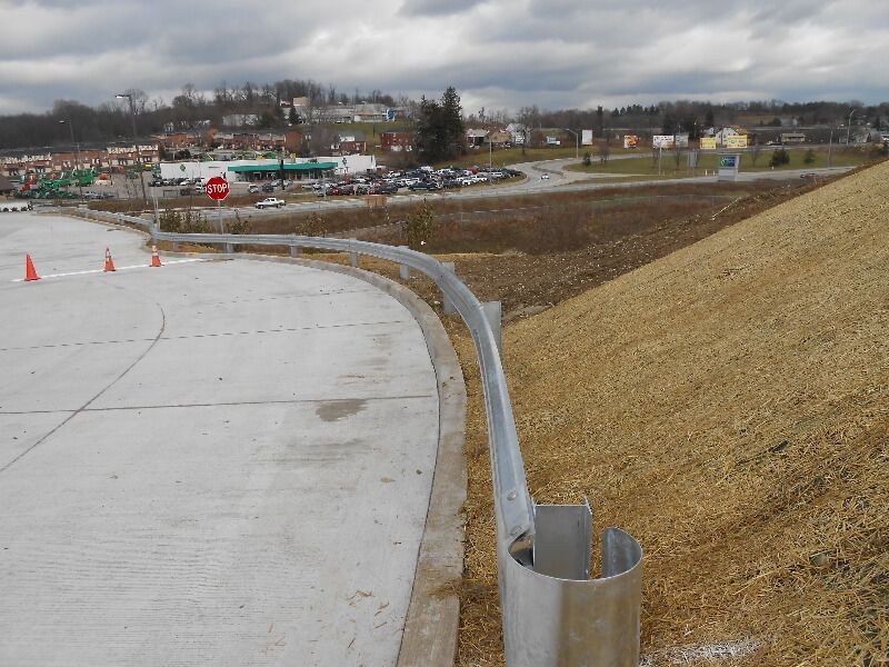 Curving roadside barrier beside a concrete path and grassy slope under cloudy skies