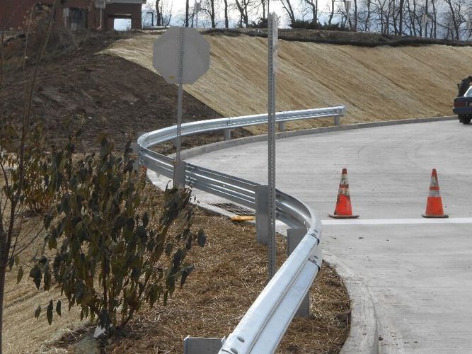 Curved roadside guardrail beside a concrete road with orange traffic cones and a blank signpost