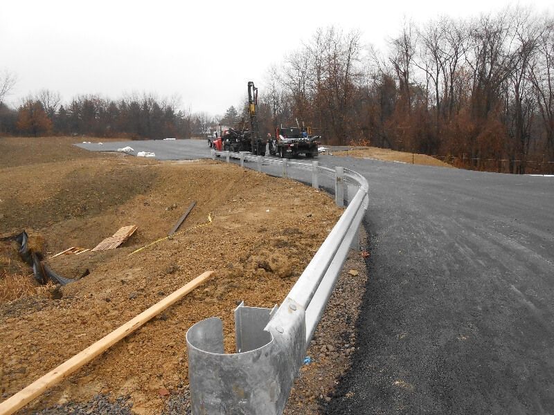 Curving road under construction with metal guardrail on a wooded roadside