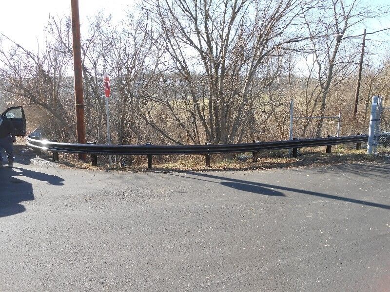 Rural roadside with black guardrail and bare trees on a sunny day