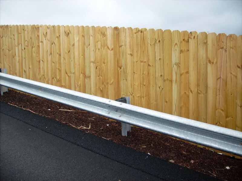 Wooden privacy fence behind a silver guardrail along a paved roadside