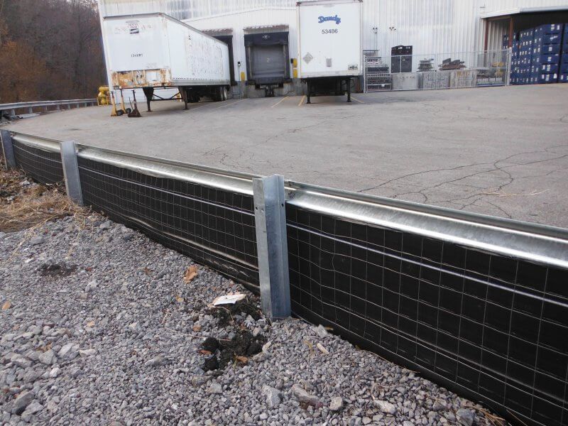 Gravel lot with a metal mesh barrier in the foreground and white industrial trailers in the background