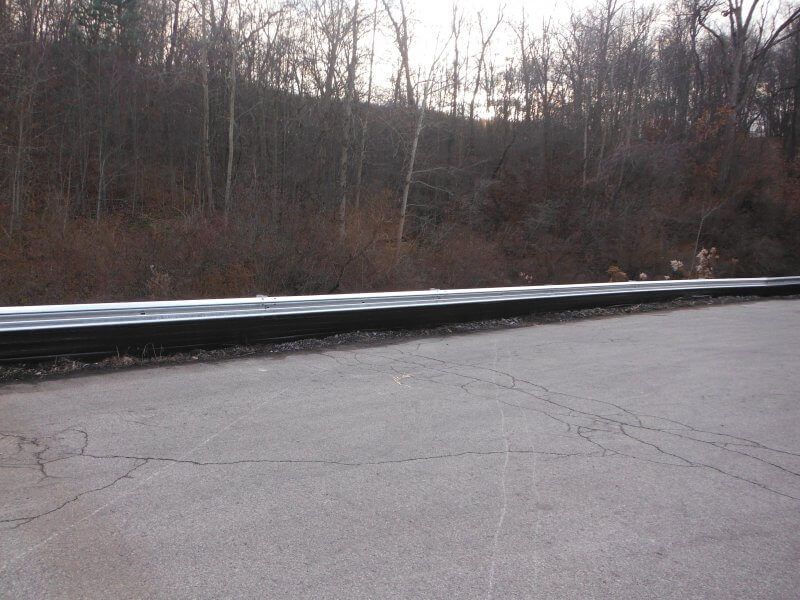 Empty roadside with metal guardrail beside a wooded embankment on a cloudy day