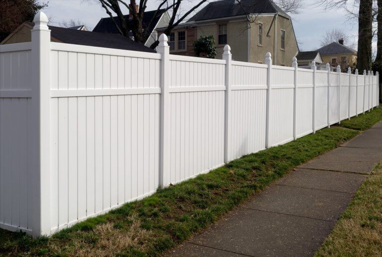 White vinyl privacy fence along a sidewalk beside houses on a cloudy day