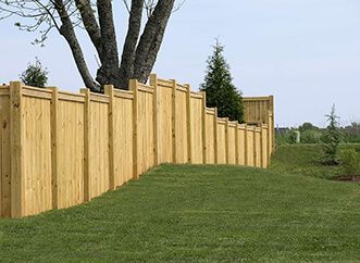 Curved wooden fence along a grassy yard beside trees under a cloudy sky