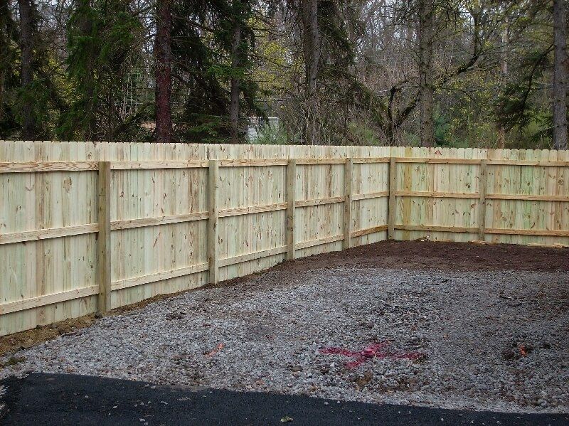 Fresh wooden privacy fence around a gravel yard with trees in the background.