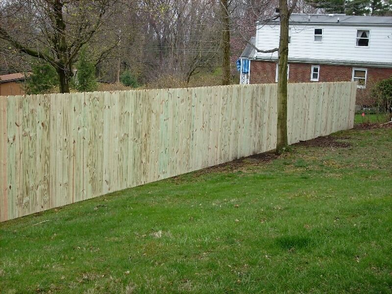 Wooden privacy fence along a grassy yard beside a house and bare trees