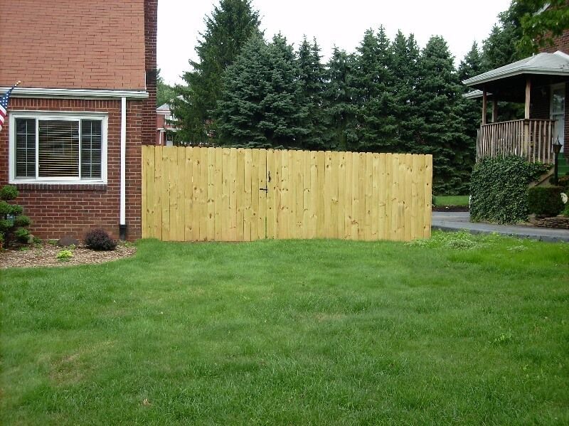 Backyard with green lawn, wooden fence panel, brick house, and evergreen trees