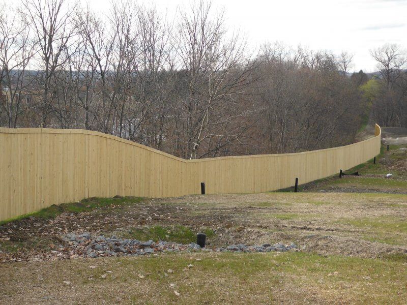 Long tan wooden fence curving along a grassy, leafless hillside under an overcast sky