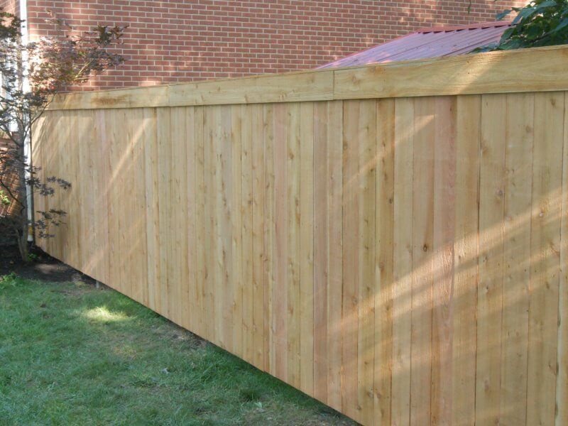 Wooden privacy fence along a grassy yard beside a brick house