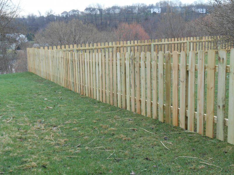 Long wooden picket fence along a grassy field under an overcast sky