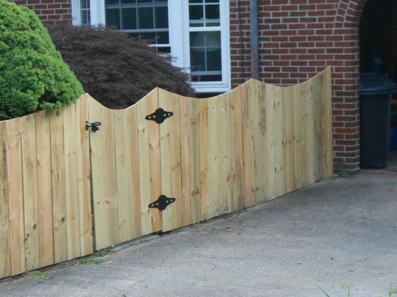 Curved wooden fence with black hinges beside a brick house and driveway
