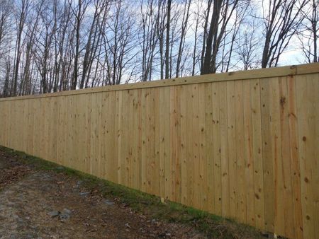 Long wooden privacy fence along a dirt path with bare trees behind it