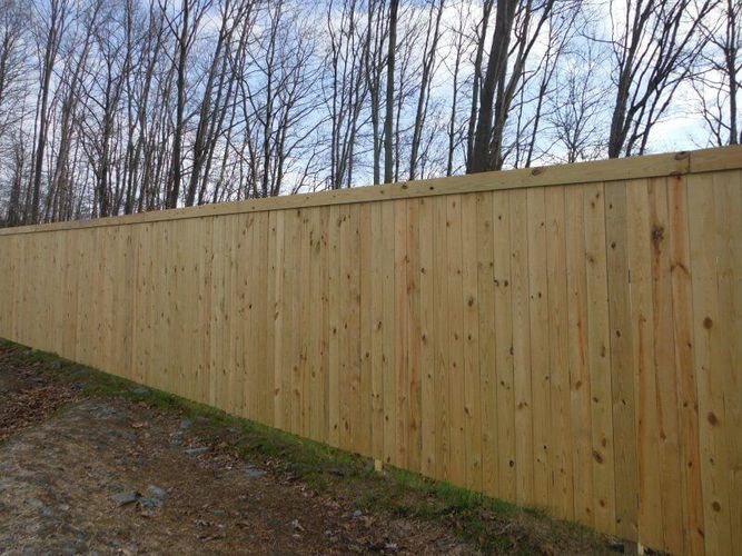 Long wooden privacy fence along a dirt path beside leafless trees