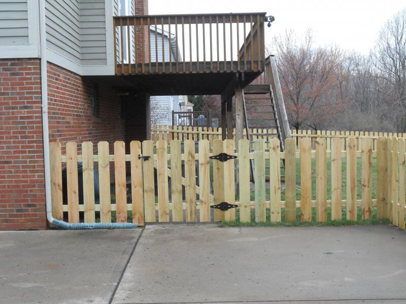 Wooden fence blocking a driveway beside a brick house and elevated deck