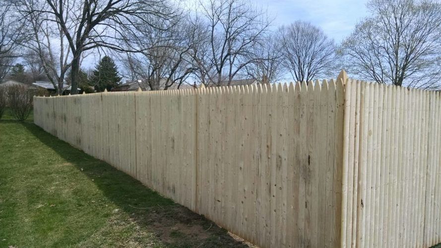 Tall wooden privacy fence along a grassy slope with leafless trees in the background