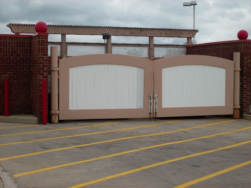 Beige double gate with white panels at a brick entrance, marked parking lot in front.