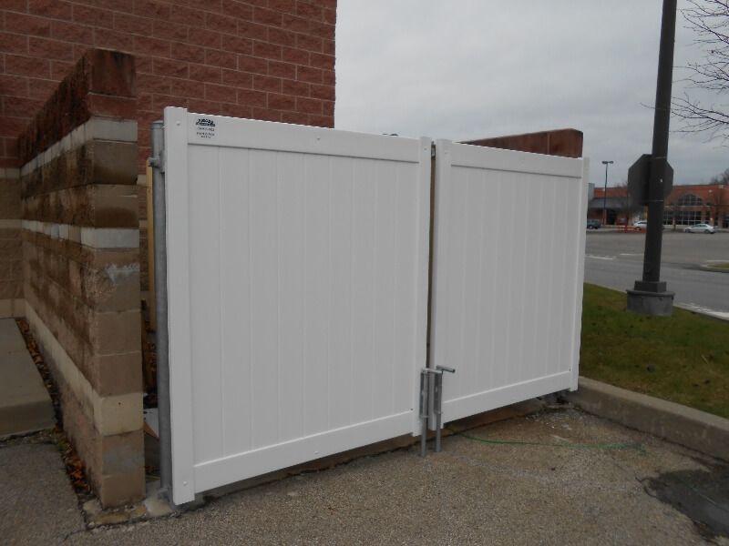 White metal fence gates beside a brick building on a sidewalk near a road
