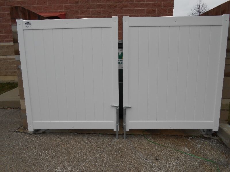 Two white fence gates closed in front of a brick building
