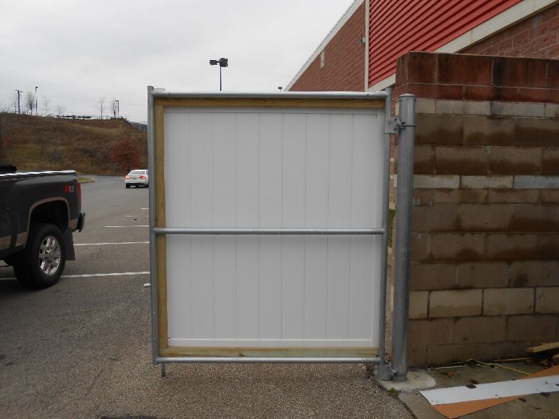 White metal gate beside a cinder block wall in a parking lot, with a truck and building in the background