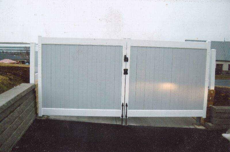White double gate with gray panels at the entrance to a paved area
