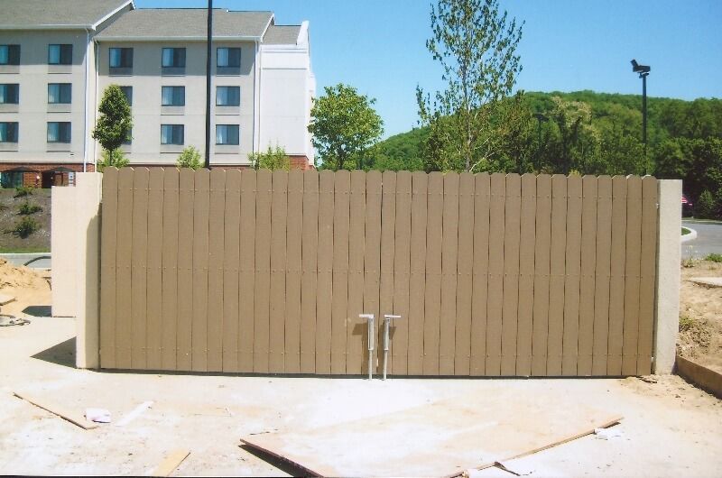 Beige wooden double gate on a paved area with apartment buildings in the background.