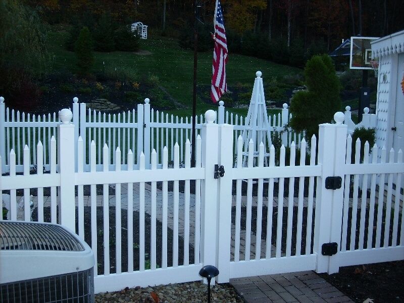 White picket fence and gate in a yard with an American flag in the background.